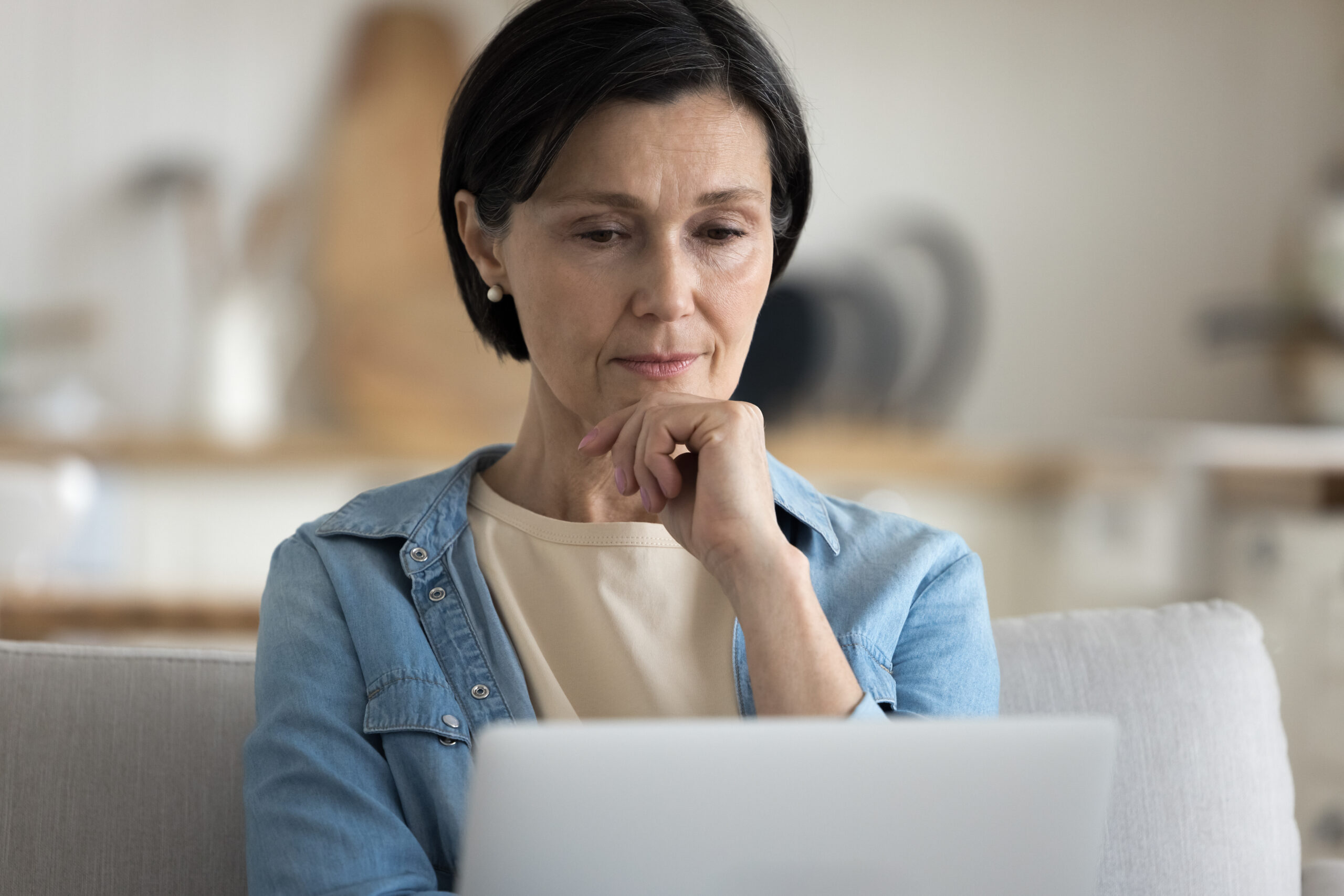 Concerned middle-aged woman looks at laptop screen, read e-mail, thinking on unpleasant news, learning about the high cost of selling the traditional way